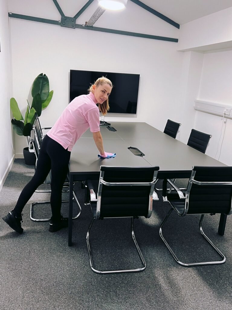 Office cleaning professional wiping a conference table in a modern meeting room.